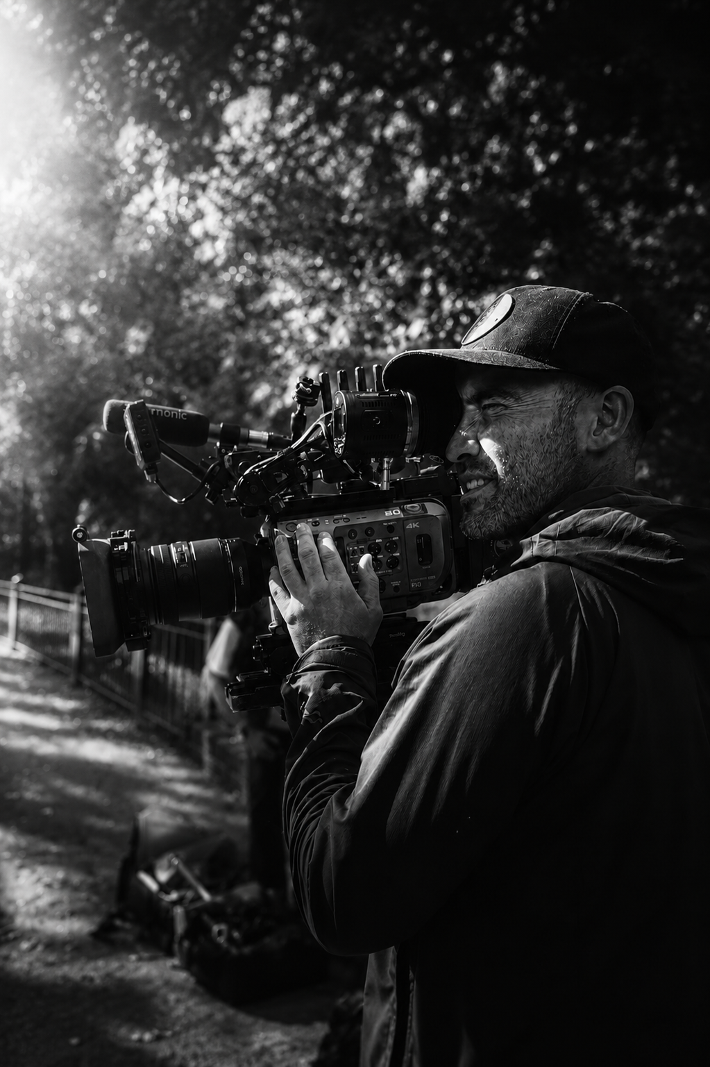 A person operating a professional video camera outdoors in the sunlight in black and white.
