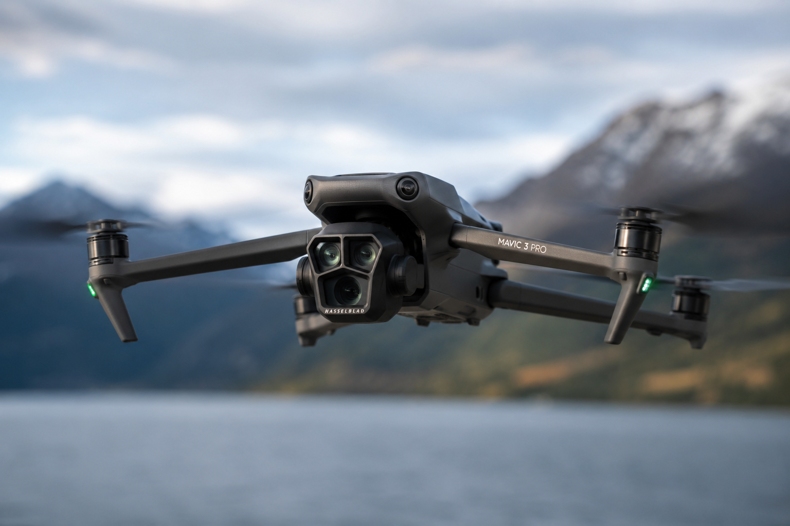 A DJI Mavic 3 Pro drone flying over a body of water with mountains and cloudy sky in the background.