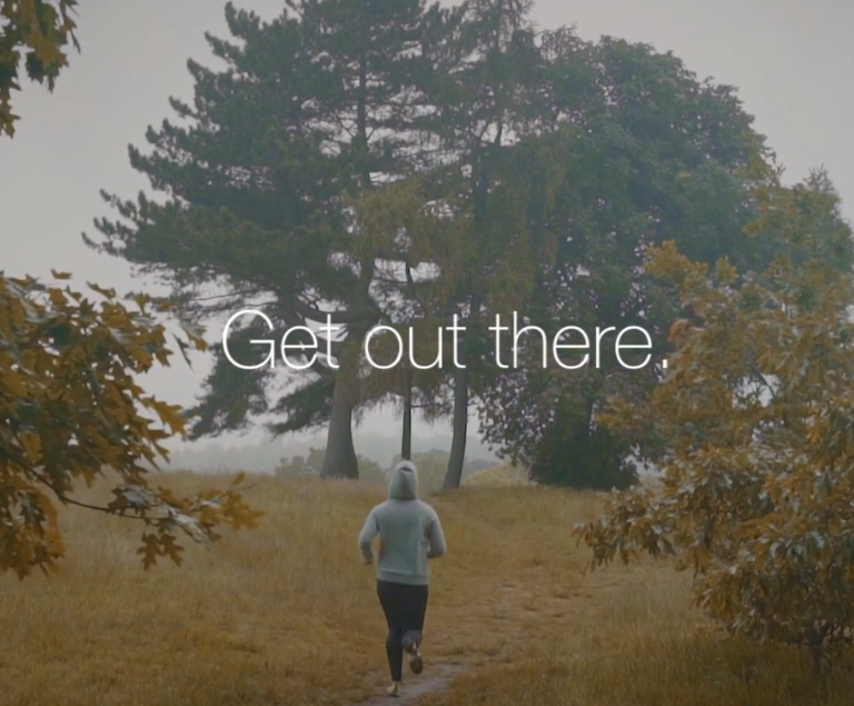 Person jogging on a trail through a park with tall trees and fall foliage, with the text 'Get out there' overlaid.