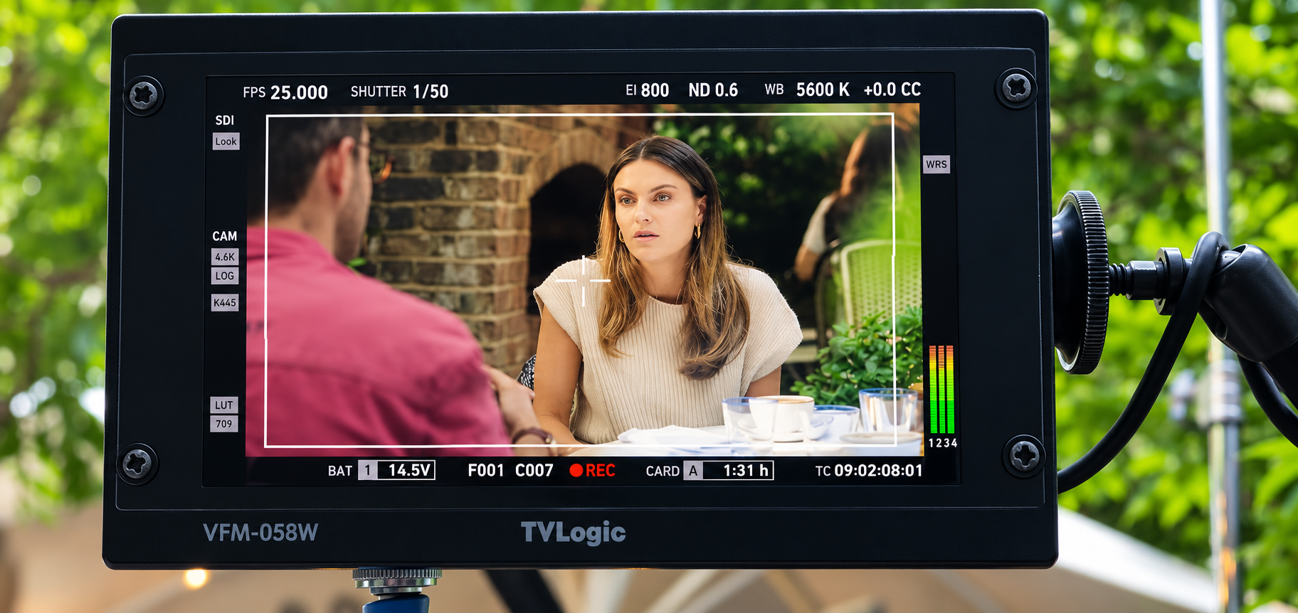 A woman and a man are having a conversation at an outdoor cafe, seen through a video camera monitor.