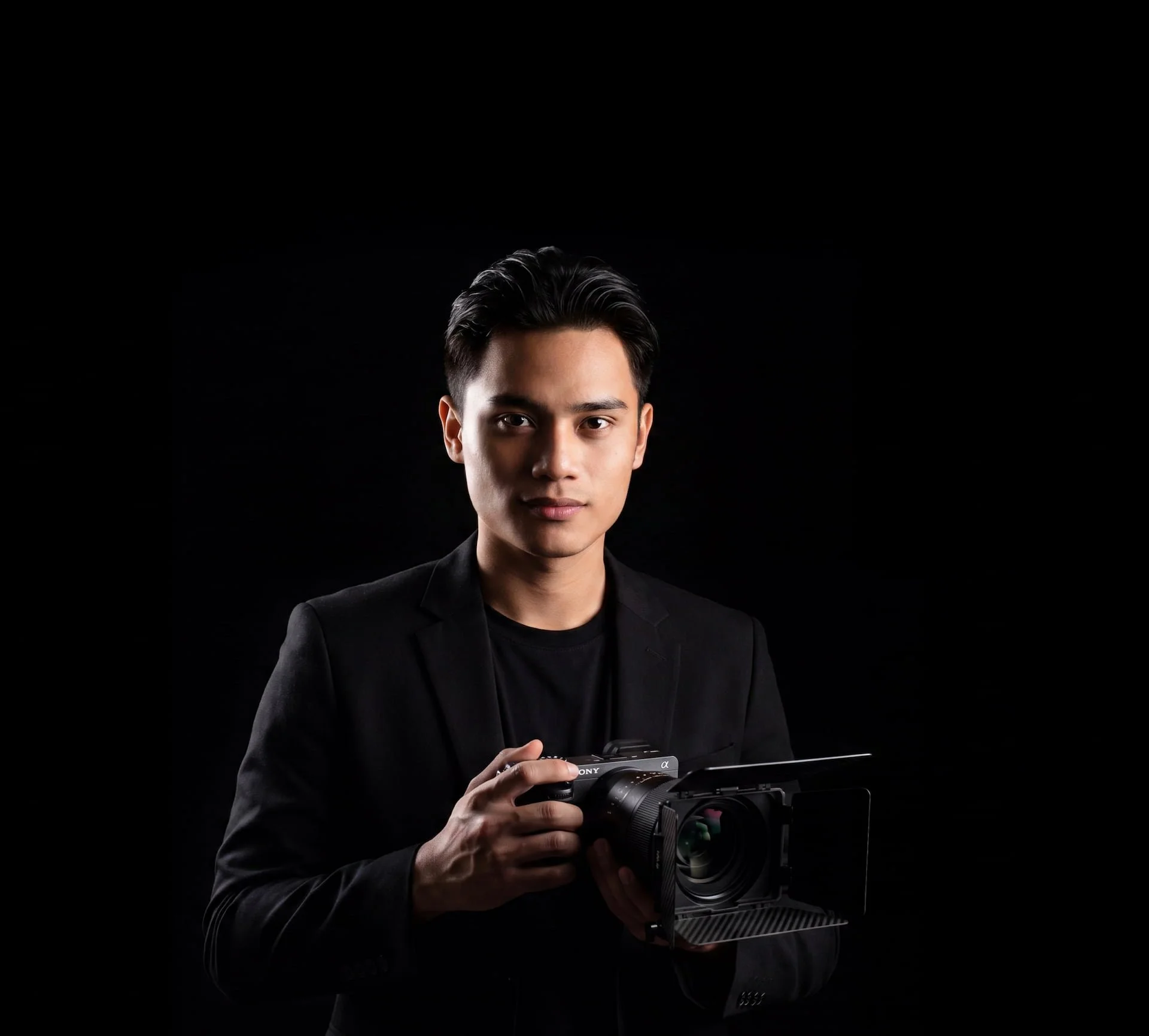 Man holding a cinematic camera against a dark background.