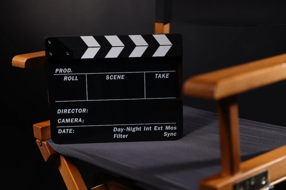 A black and white film slate on a gray surface, surrounded by wooden chairs with black cushions.