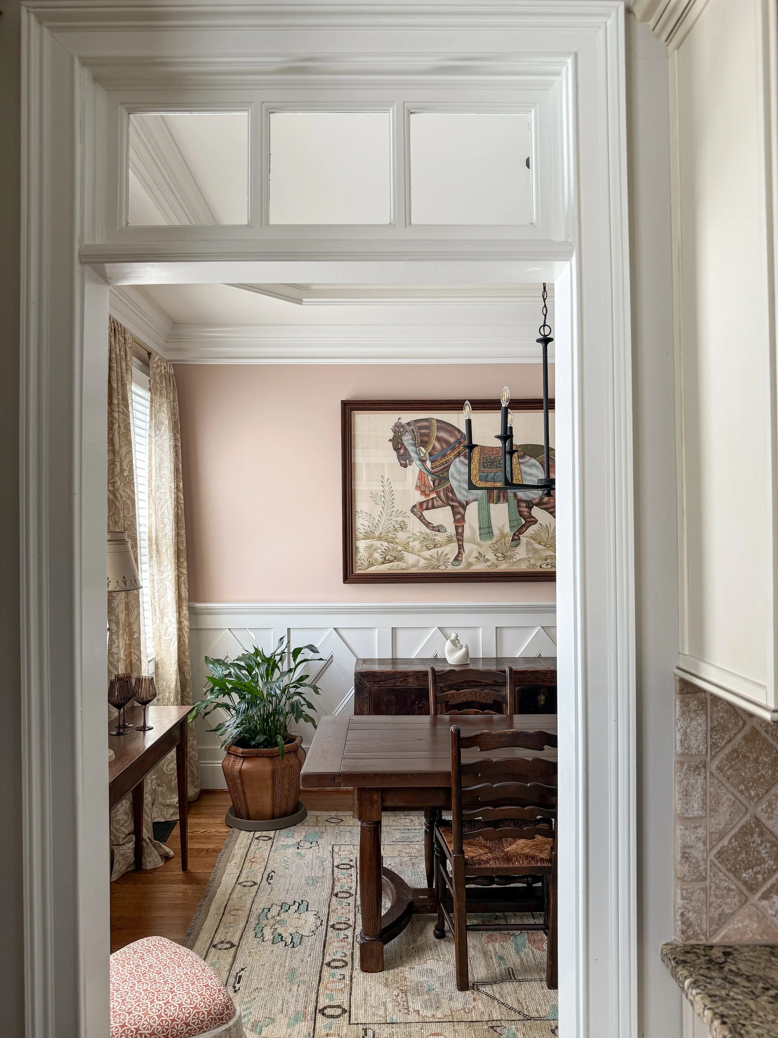 Traditional dining room with an antique table, patterned curtains, framed equestrian art, and layered furnishings.