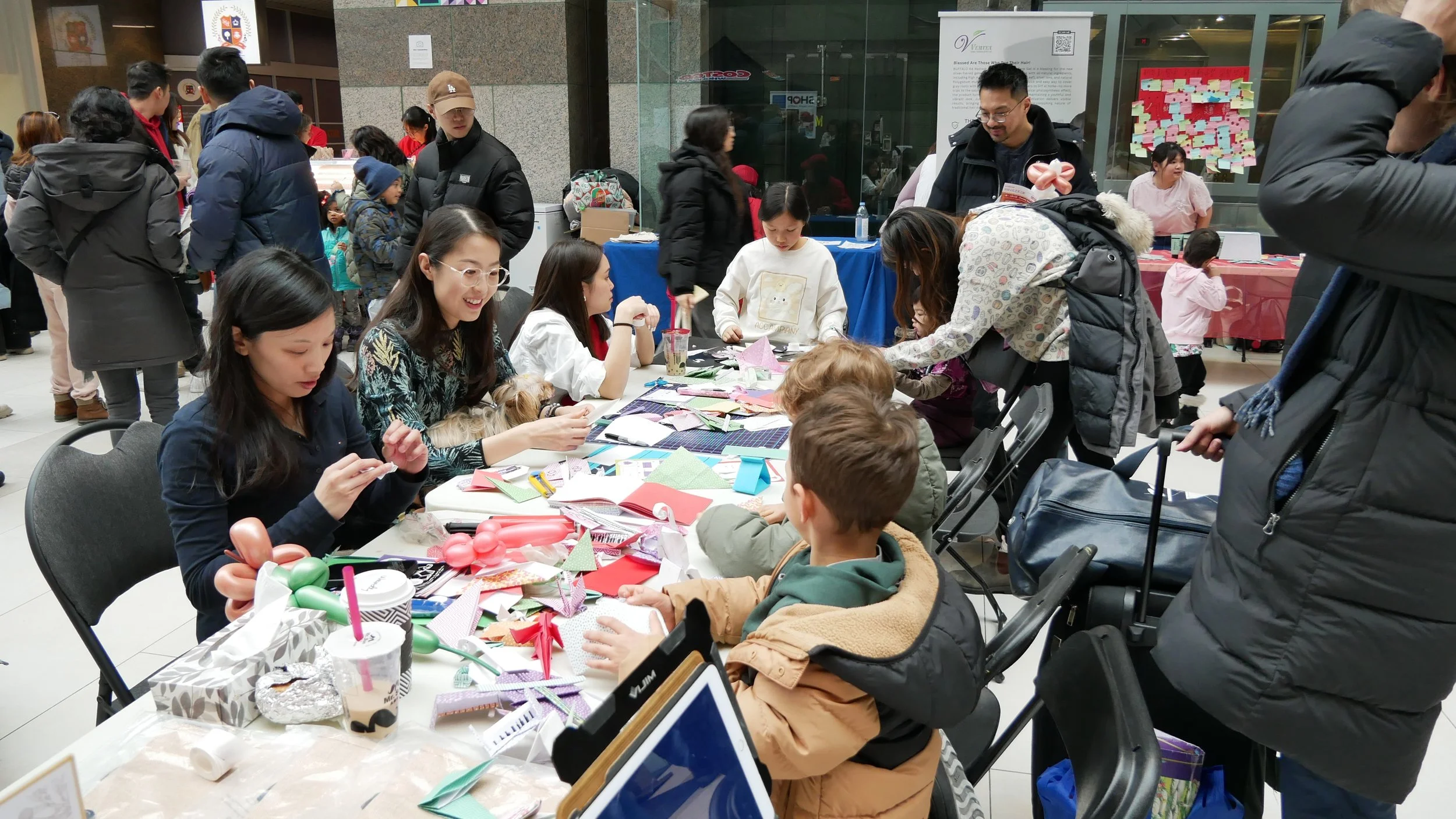 People gathered around tables making paper crafts at an indoor event.