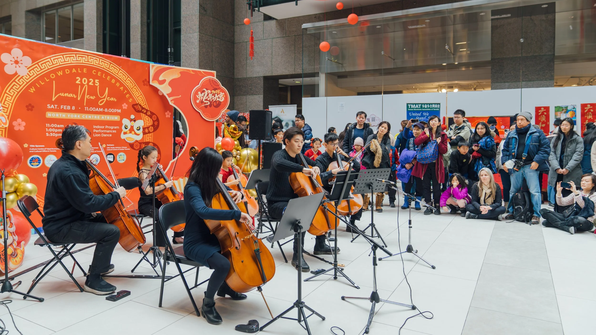 Musicians playing string instruments in a mall during a Lunar New Year celebration with a large orange and gold sign.