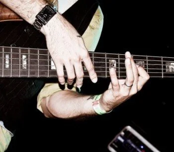 Close-up of a person playing a guitar, focusing on their hand on the fretboard.