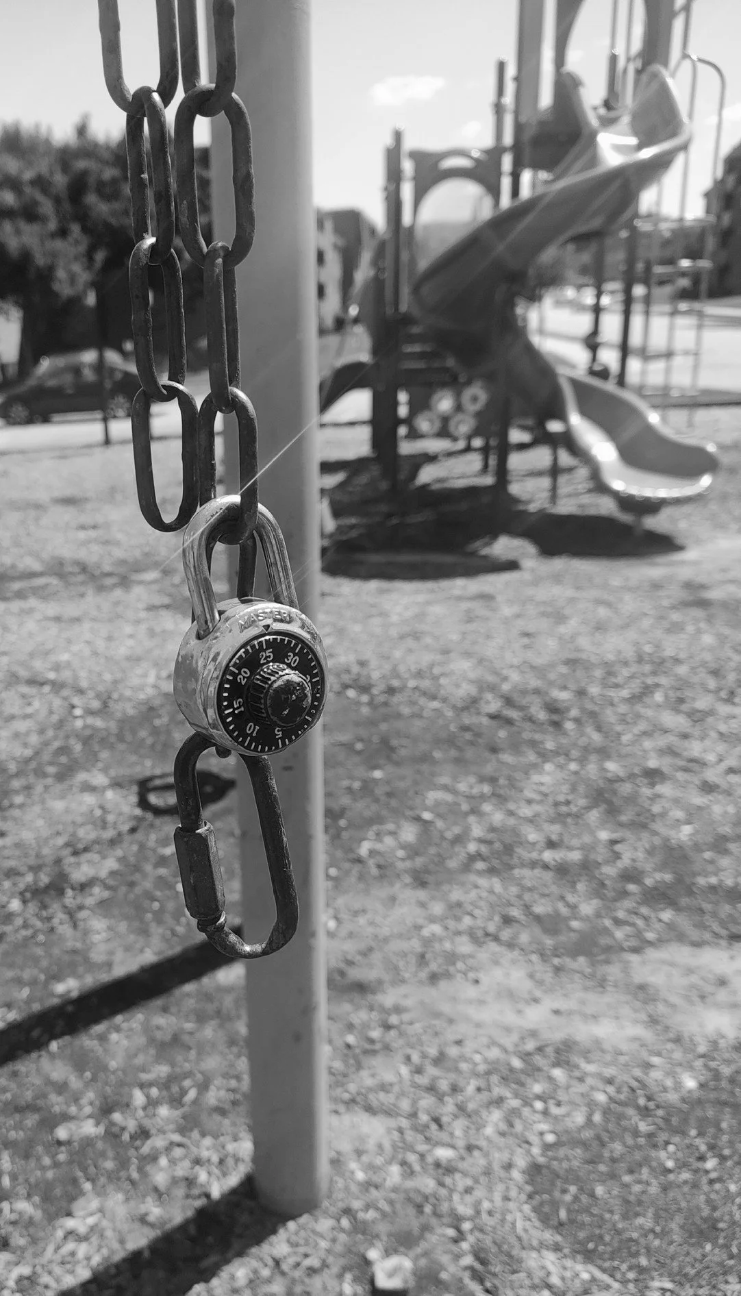 A playground with a chain and a combination lock in the foreground and a slide in the background.