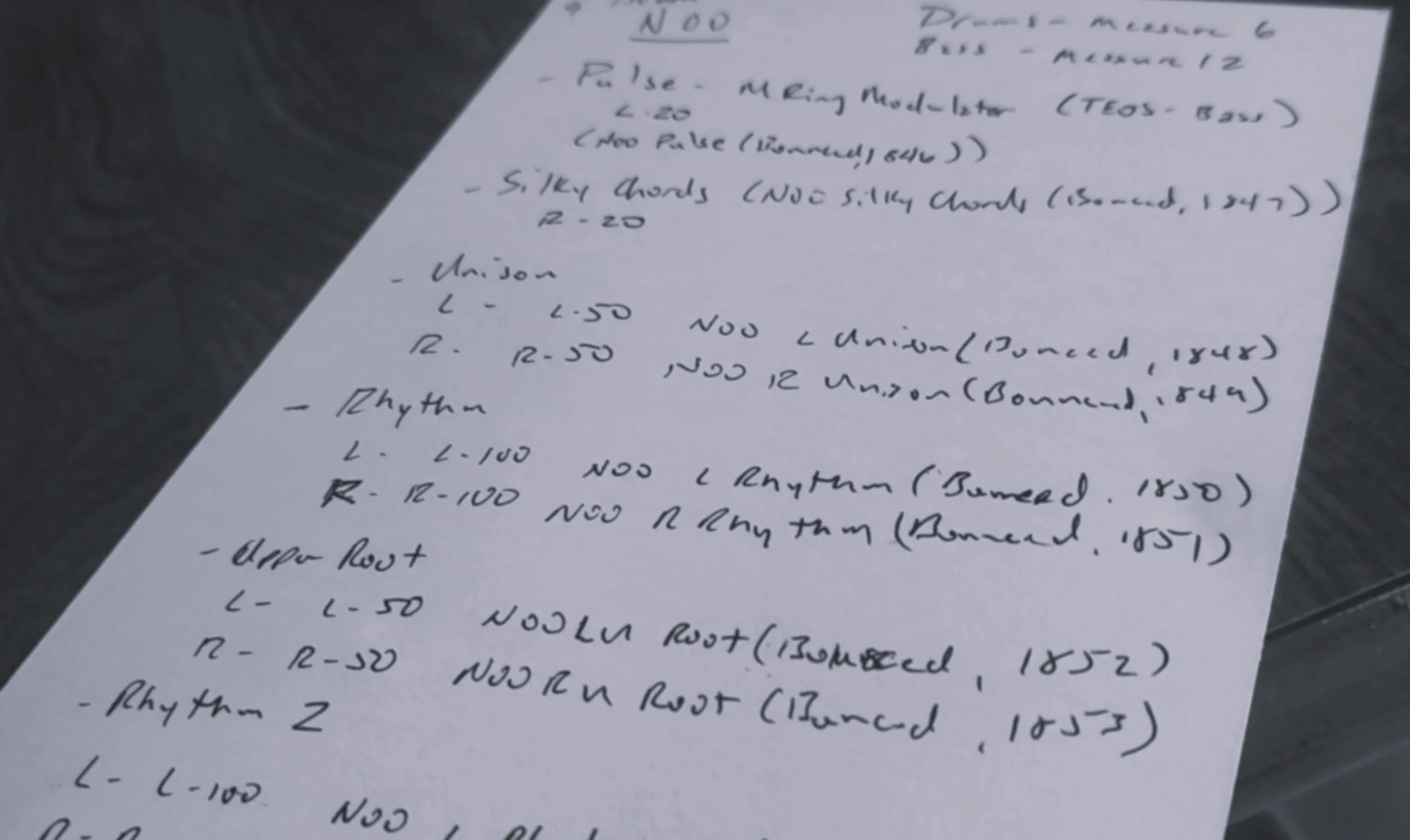 Close-up of a handwritten music notes and instructions on a sheet of paper, resting on a dark surface.