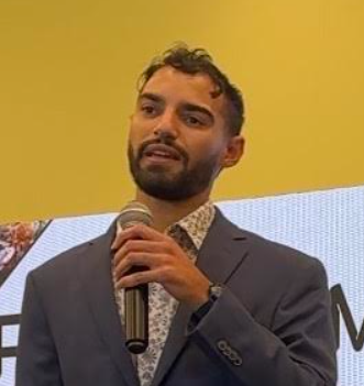 Man in a suit holding a microphone speaking at an event