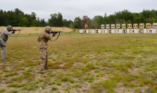 Two soldiers in camouflage uniforms aiming rifles at a shooting range with numbered targets.