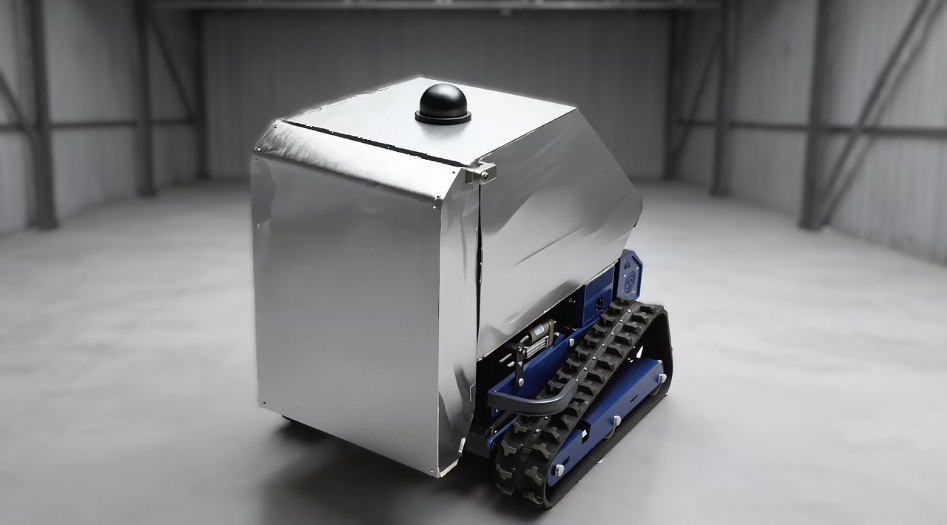 A small robotic machine with a metal body and treads, placed in an empty, well-lit industrial or storage space.