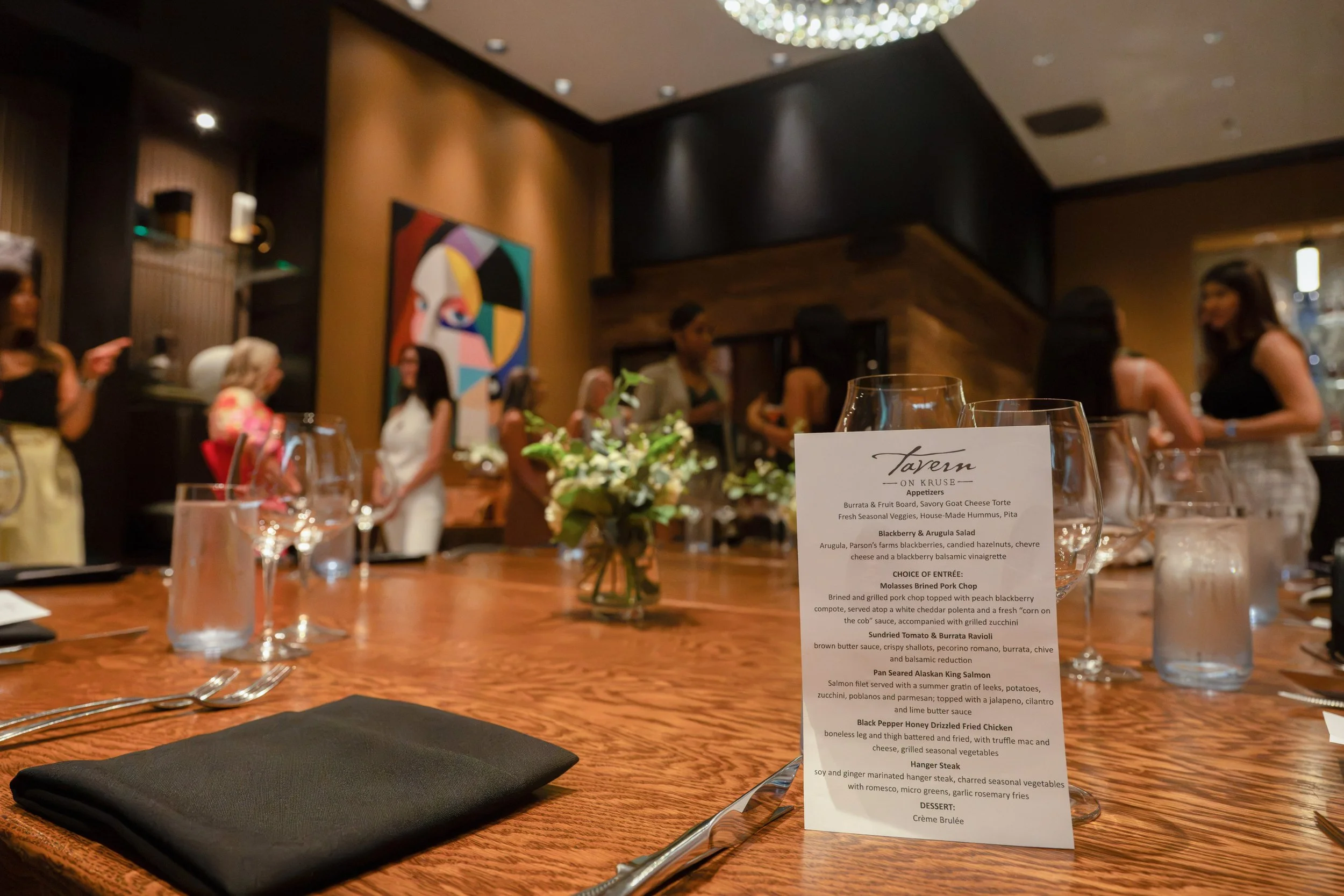 Long communal dining table set for a private event in The Annex with menu cards, glassware, and floral centerpieces.