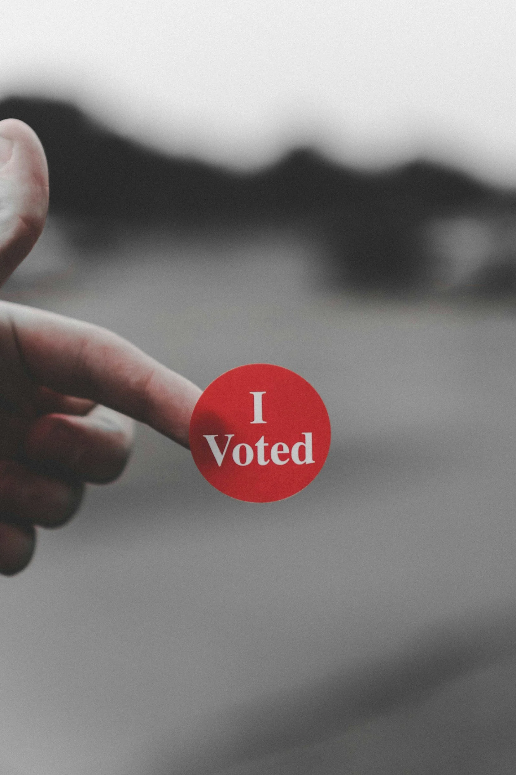 Close-up of a hand with a finger holding a red 'I Voted' sticker.