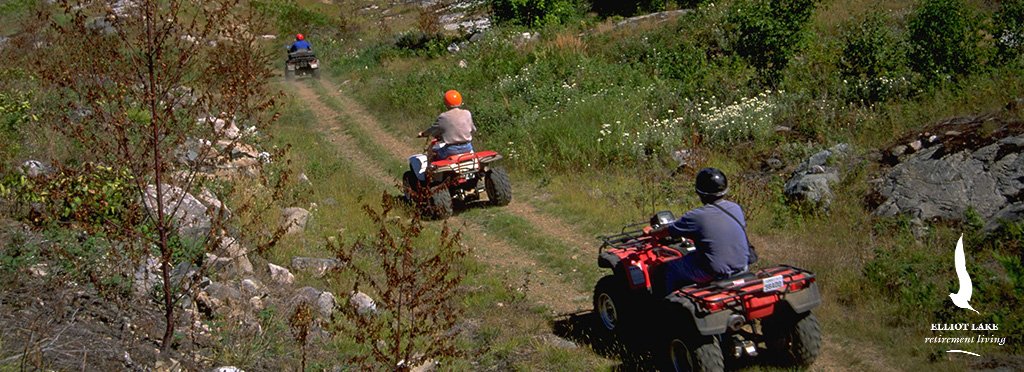 Three people riding all-terrain vehicles along a dirt trail through a forested area.