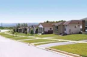 Row of suburban houses with neatly maintained lawns under a clear blue sky.