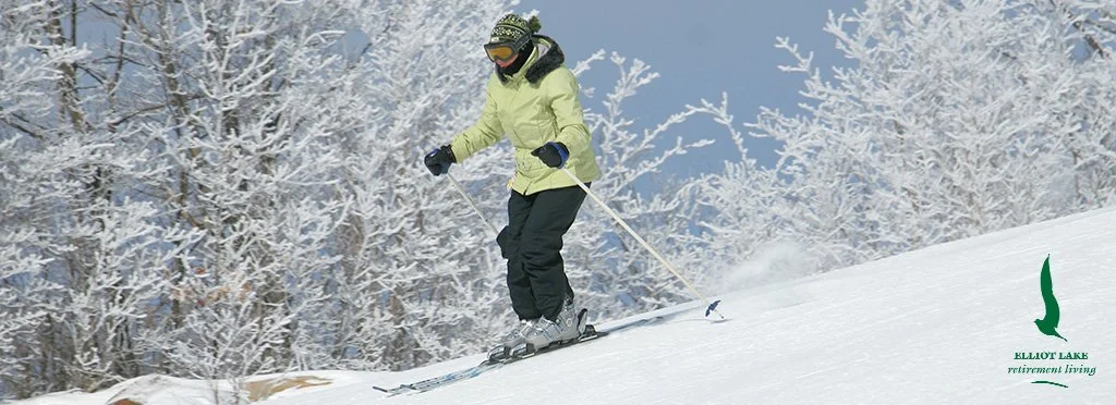 Person skiing down a snowy slope with snow-covered trees in the background at Elliot Lake.