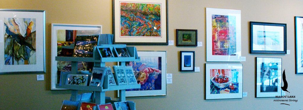 Gallery wall with various framed colorful artworks and photographs, and a blue display rack with postcards or small prints.