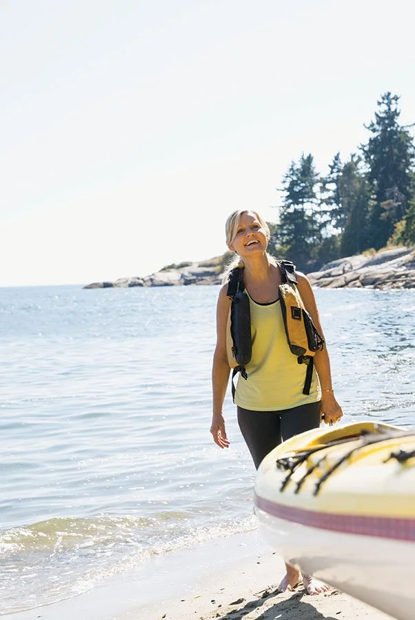 A woman carrying a kayak along a lake shoreline