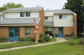 Apartment building with brick and beige siding, multiple entrances, and a Canadian flag in front.