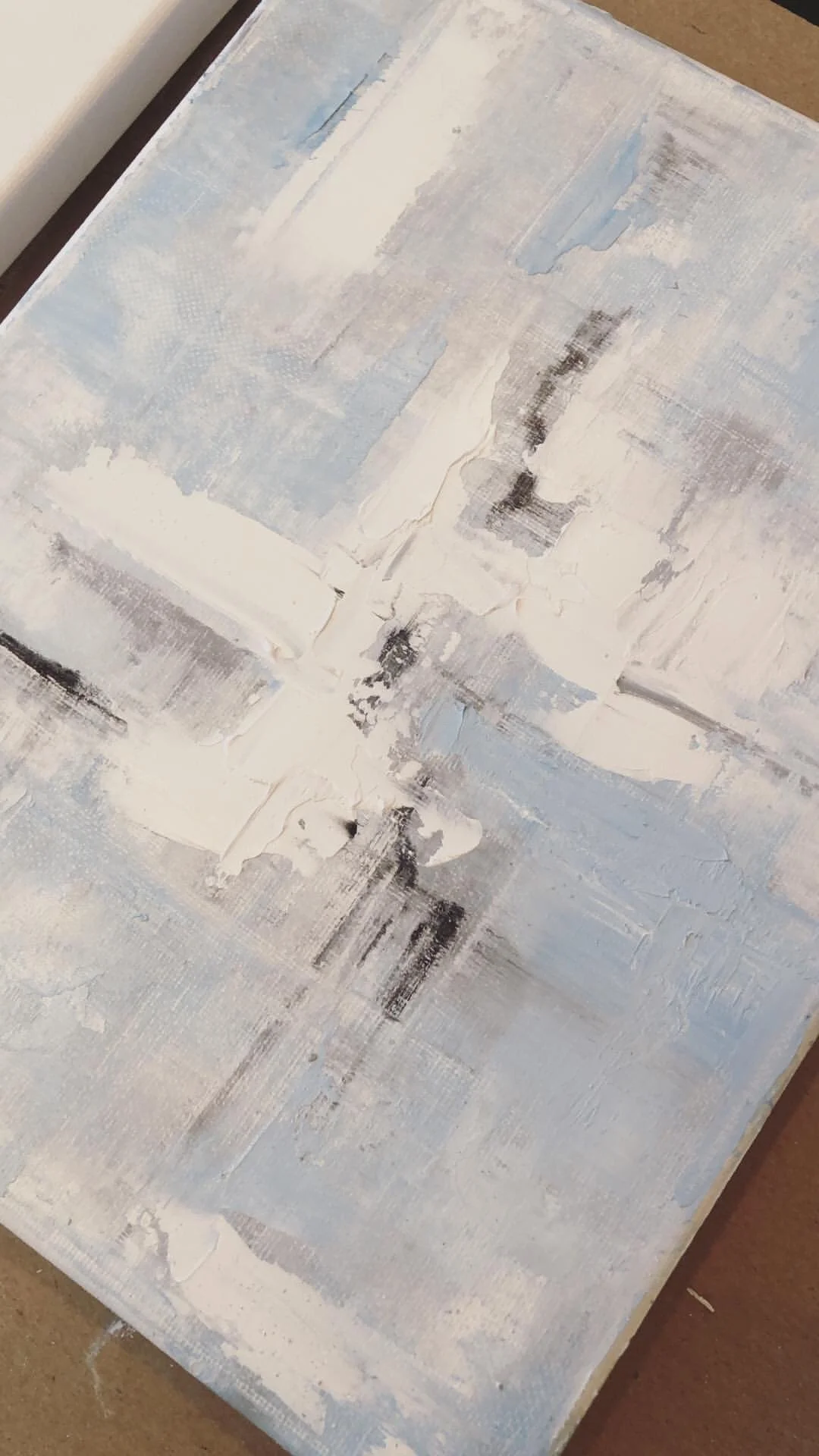 An abstract, textured painting with shades of blue, white, gray, and black applied with visible brushstrokes.