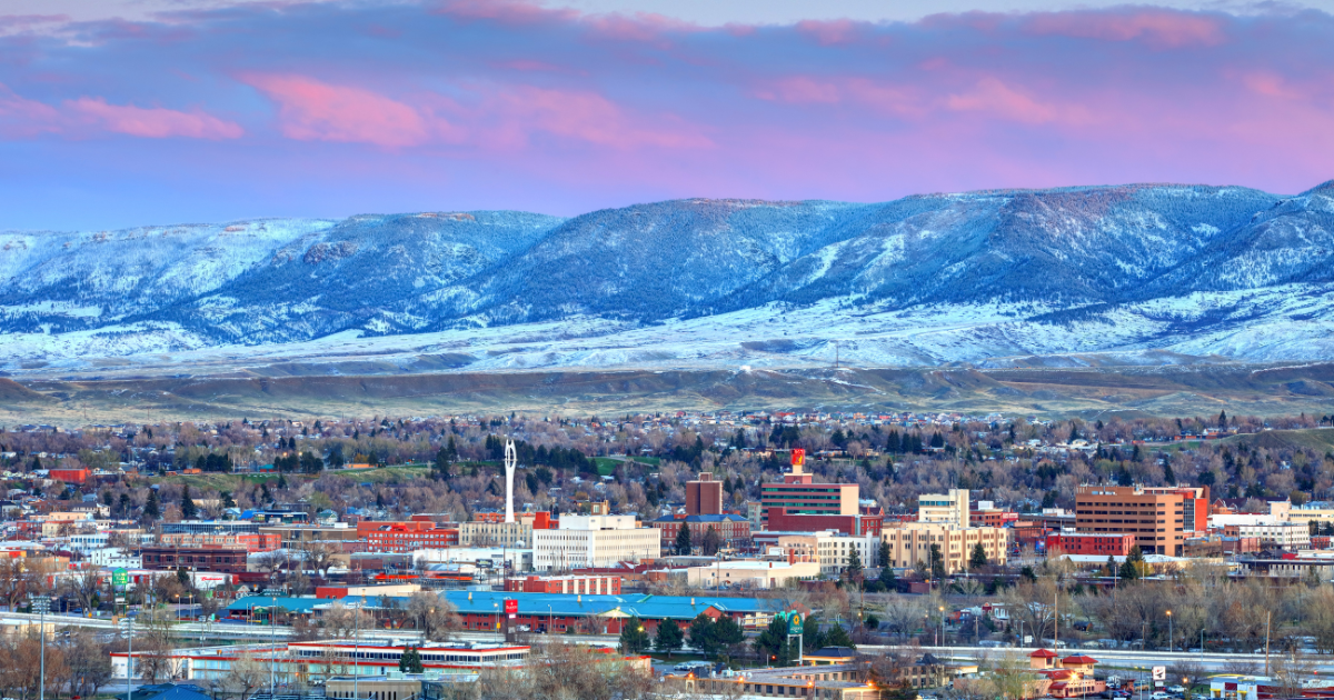 Casper cityscape with snow-capped mountains in the background, buildings in the foreground, and a colorful sky with pink and blue hues.