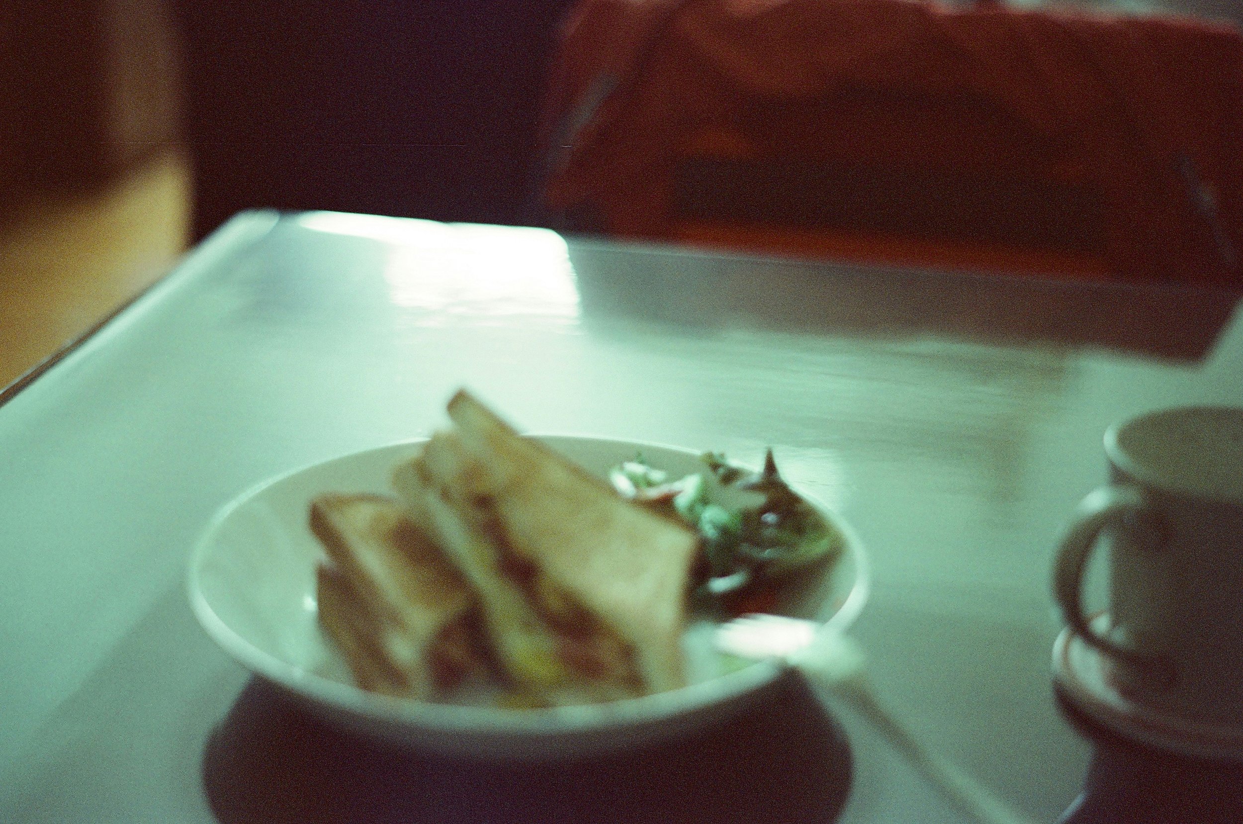Close-up of a small, white plate with a sandwich on a white table, with a blurred background.