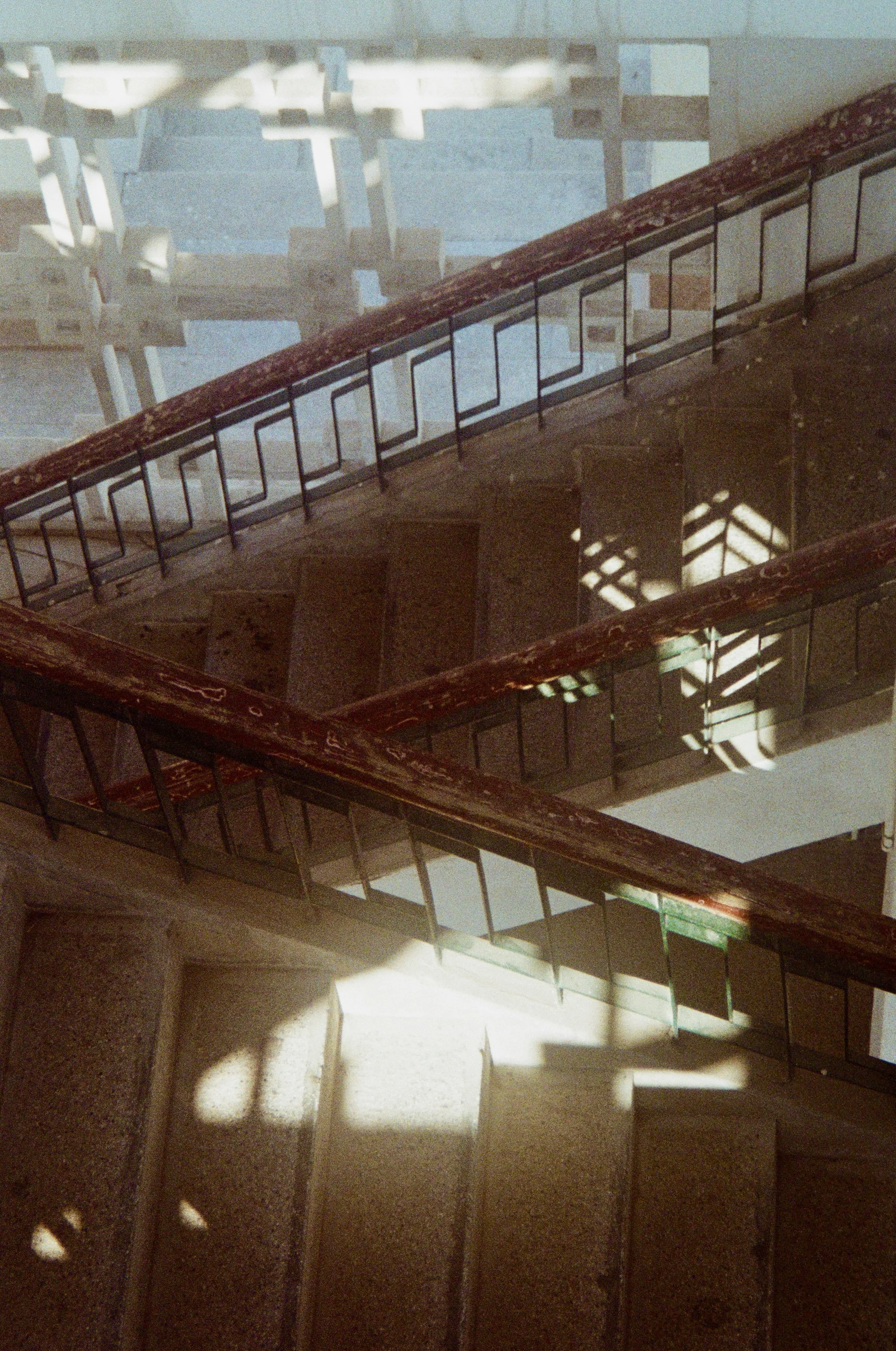 Shadow of stair railing cast on a carpeted staircase and wall with sunlight streaming through a window.