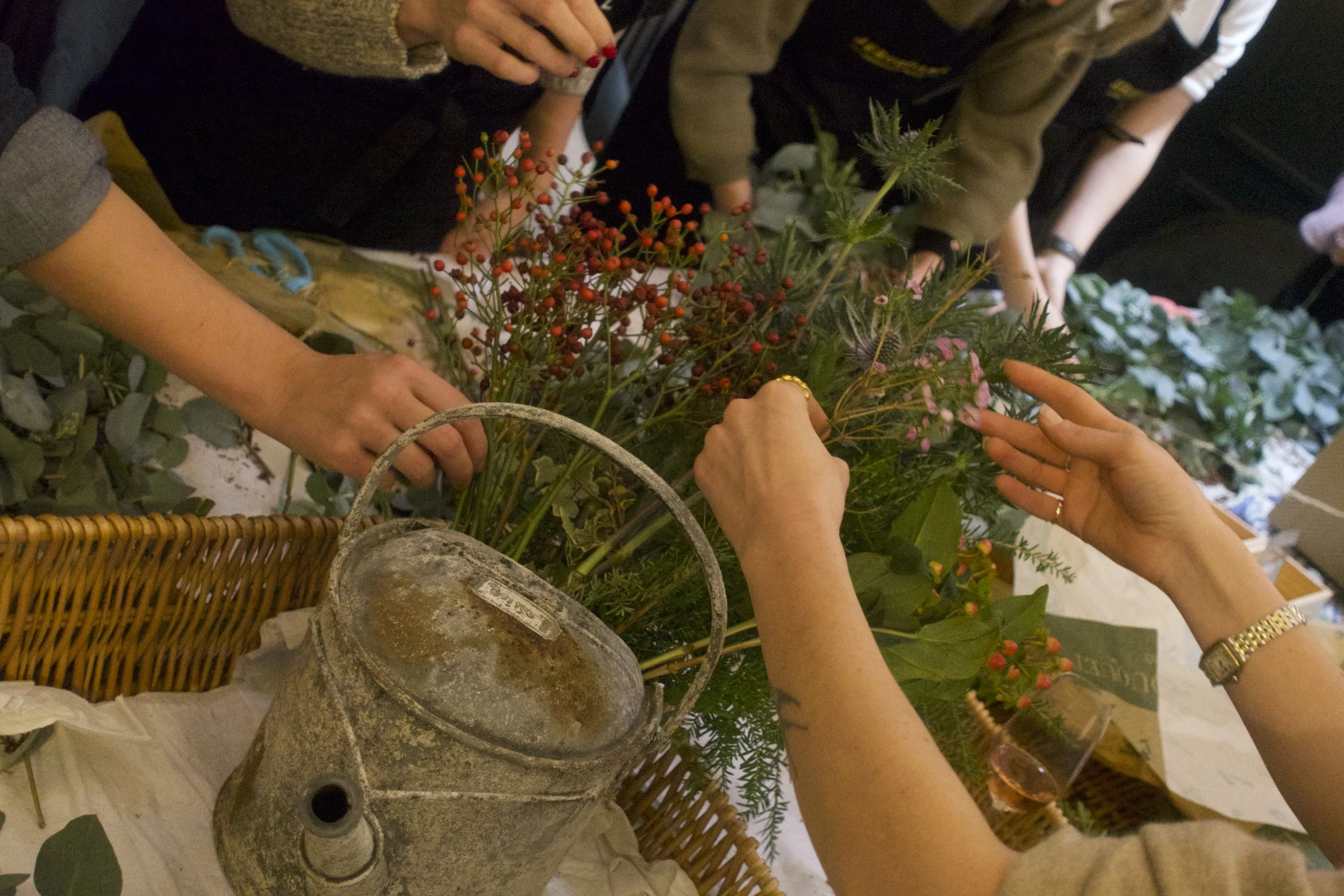 People arranging and creating floral arrangements with various flowers and greenery on a table.