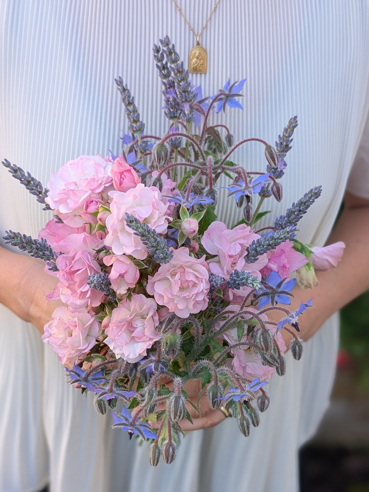 Person holding a bouquet of pink carnations and purple borage flowers against a ribbed cream-colored background.