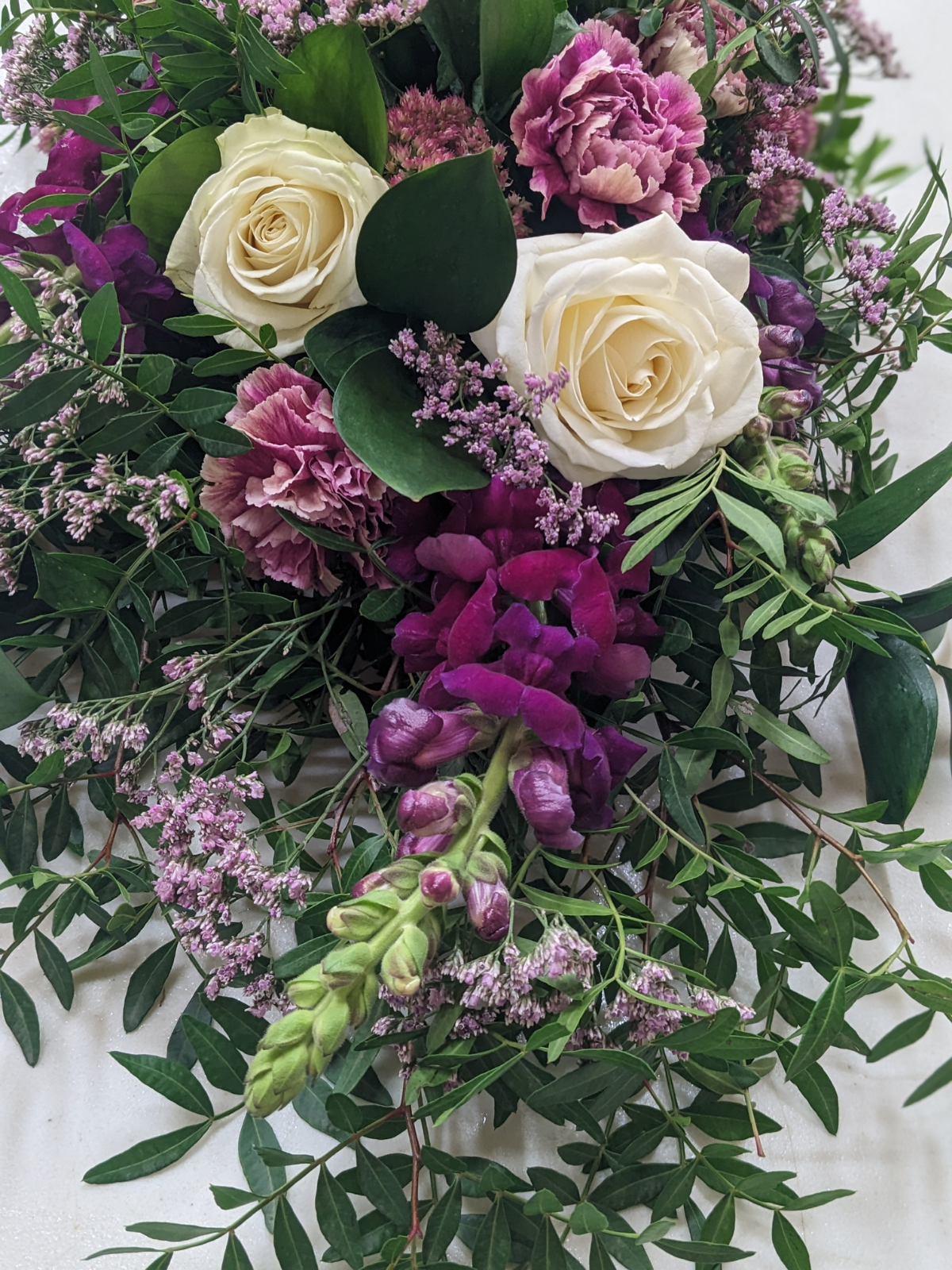 A floral arrangement with white roses, purple carnations, lavender, and green foliage.
