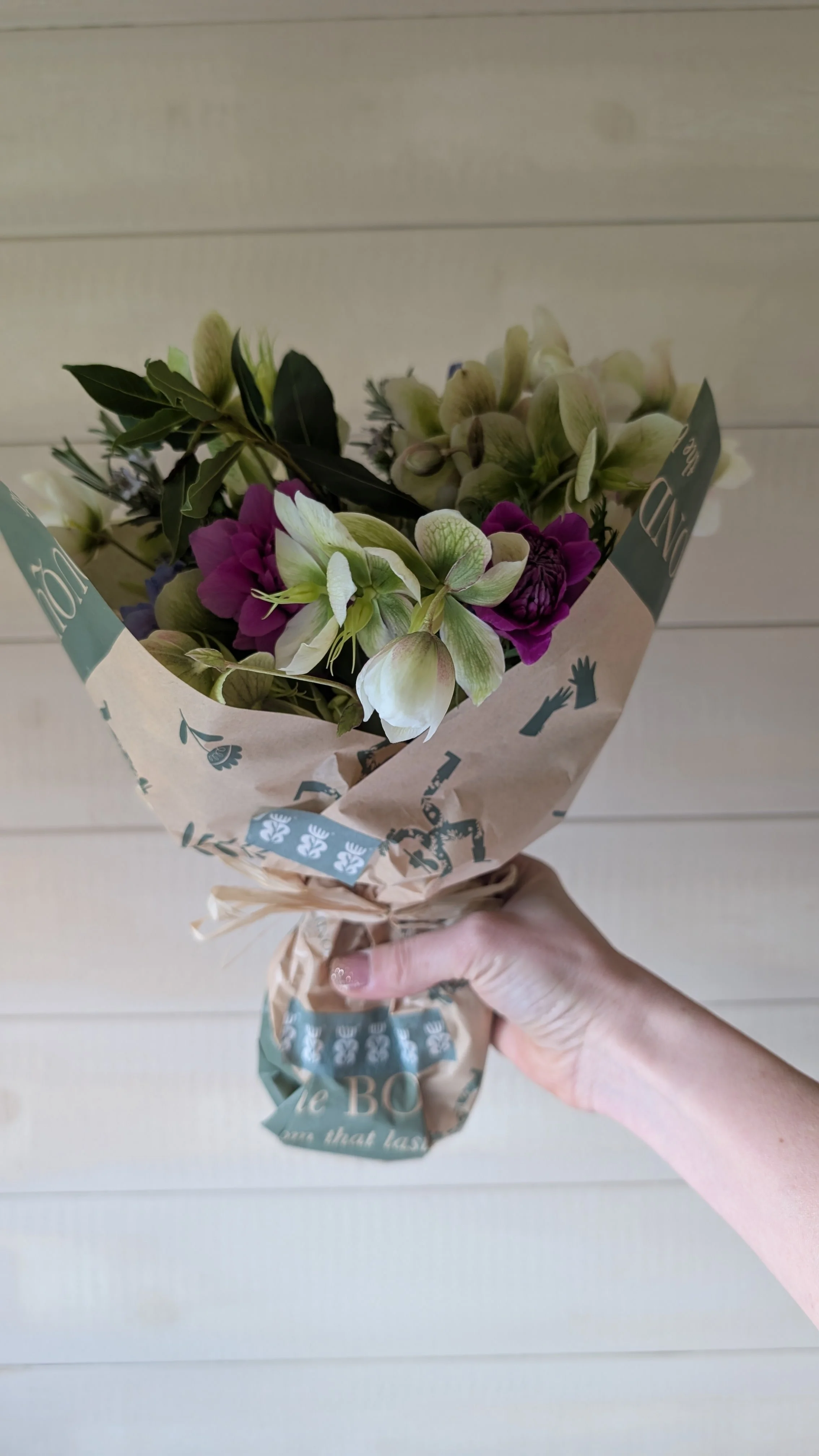 A hand holding a small bouquet of mixed flowers wrapped in decorative paper with a white background.