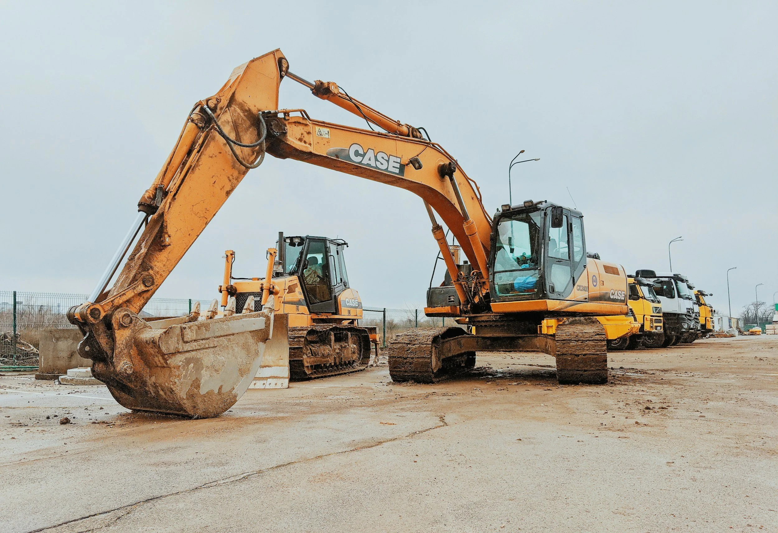 Row of construction excavators and trucks on a construction site during daytime.