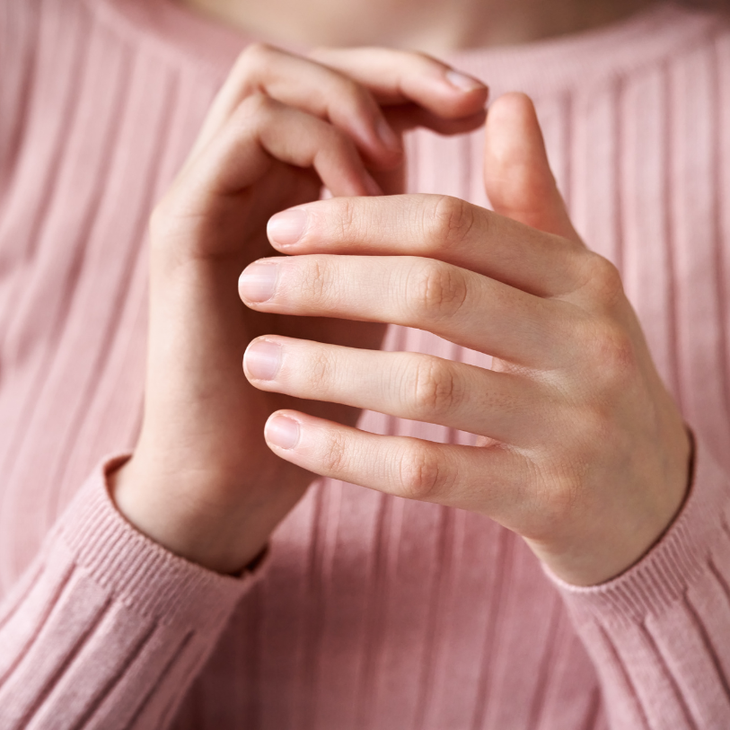 Close-up of a person wearing a pink ribbed long sleeve shirt with their hands gently clasped together.