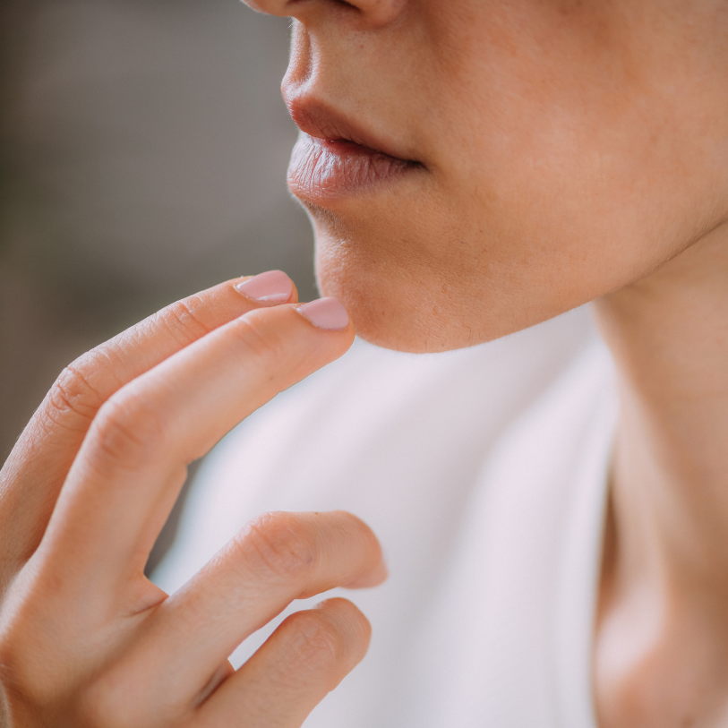 Close-up of a person touching their chin with their fingers, with a neutral expression.