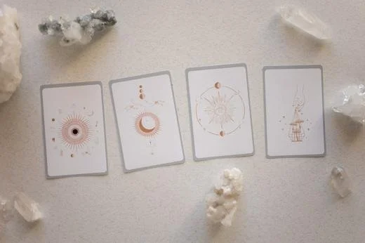 Four tarot cards laid out on a white surface surrounded by crystals.