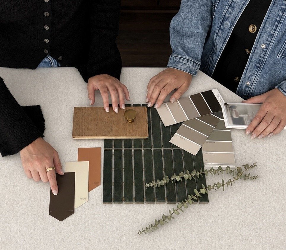 Two people are looking at various color and material samples, including wood, tile, and paint swatches, on a table.