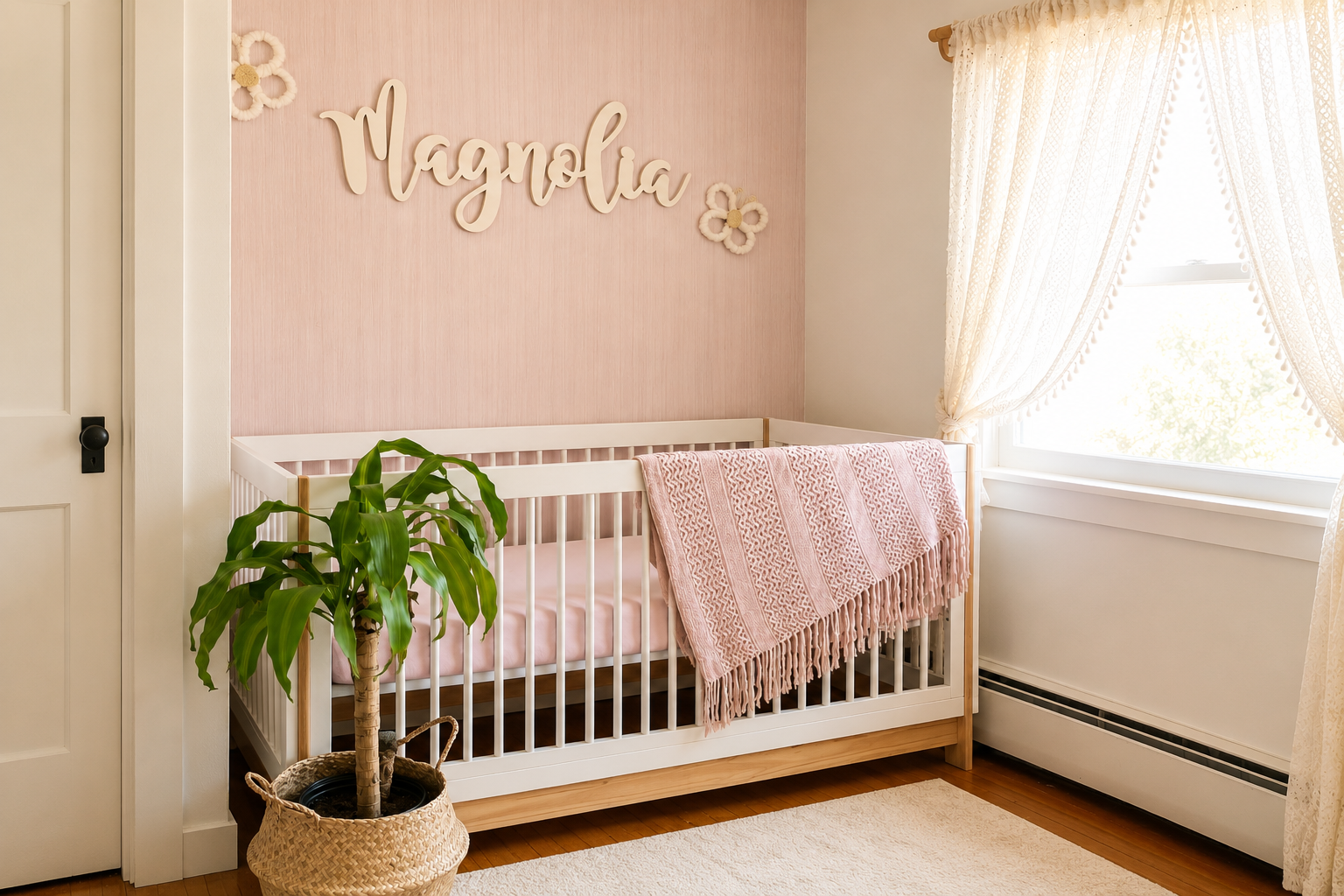 A nursery with pink wall decor, a white crib with a pink blanket, a green potted plant, and a window with cream curtains.