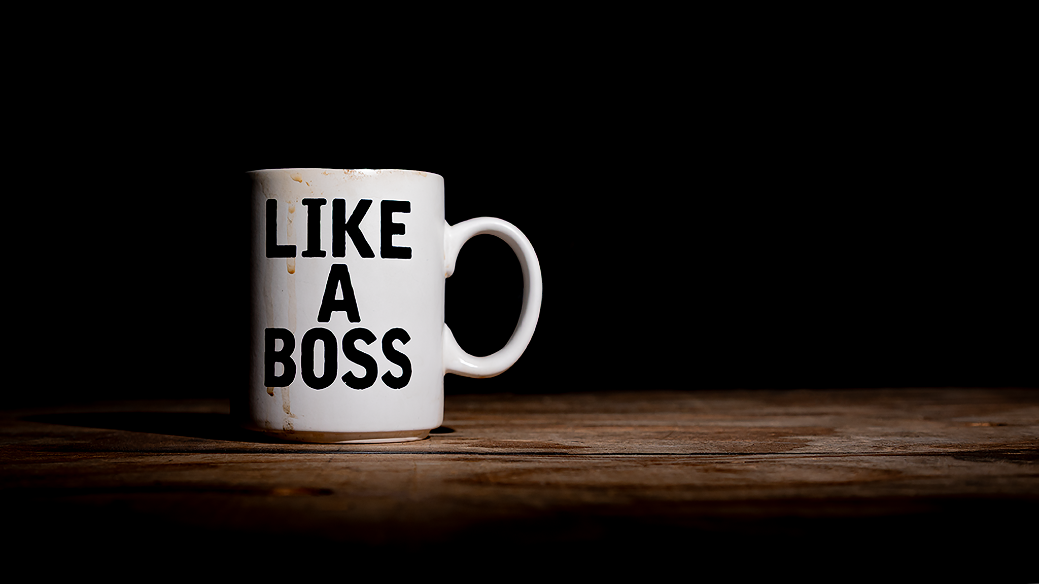White coffee mug reading "LIKE A BOSS" on wooden surface, dark background