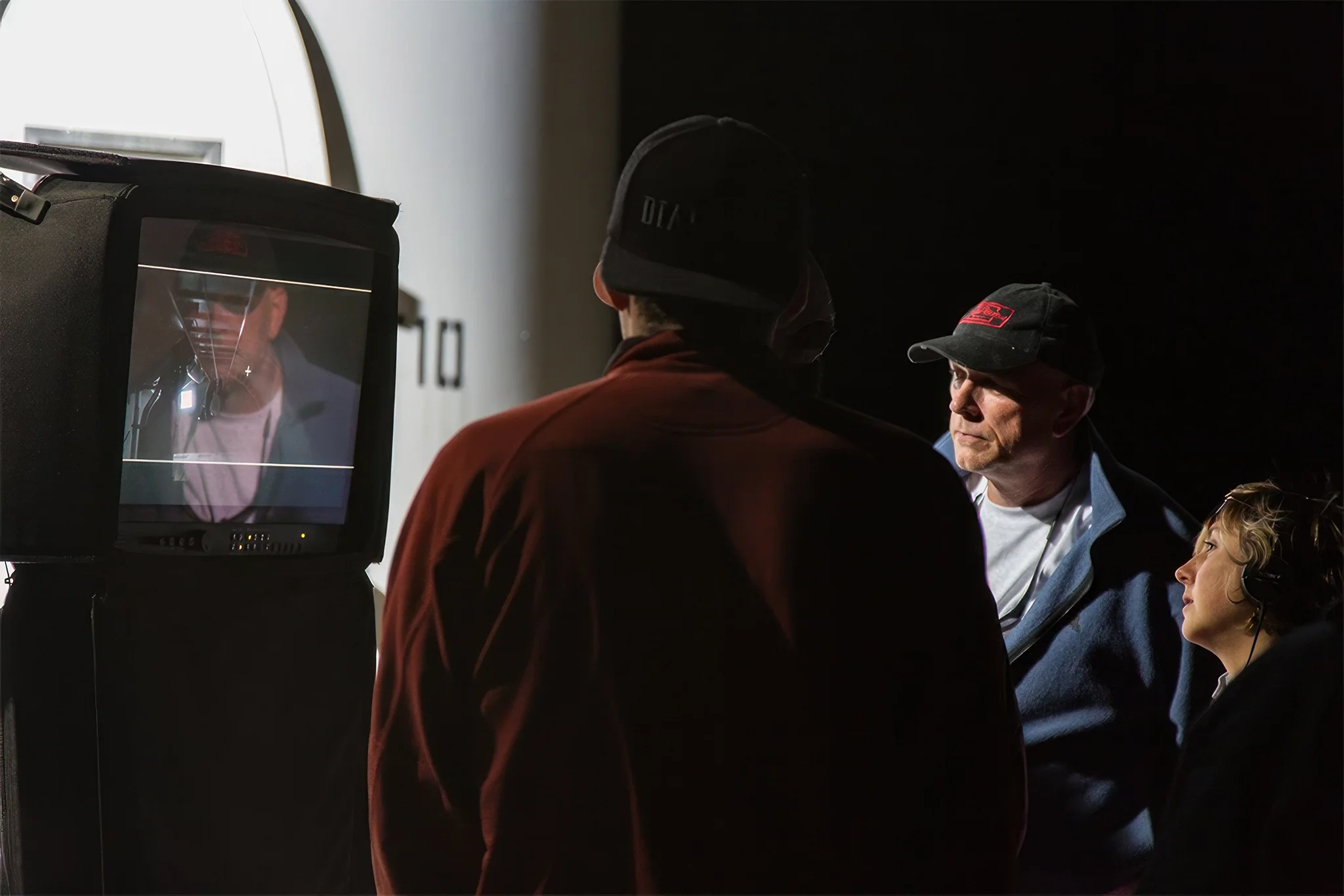 Eric Wood with crew are gathered around a monitor on Osiris film set. Eric's reflection is in the monitor, while others observe.