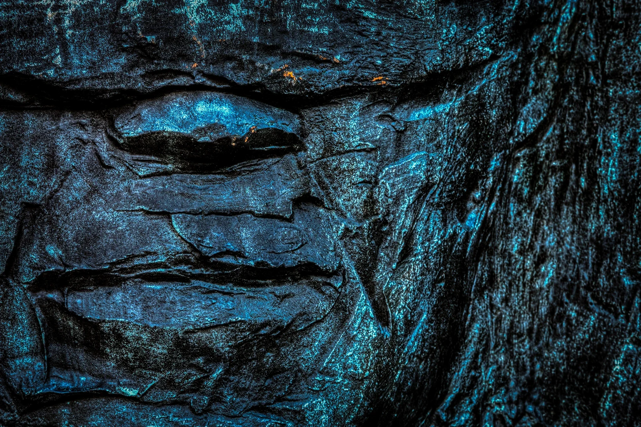 Close-up of Róbert Kreutz Memorial Plaque, Memento Park, Budapest — textured surface with blue and orange light, rough patterns and cracks, blindfolded figure