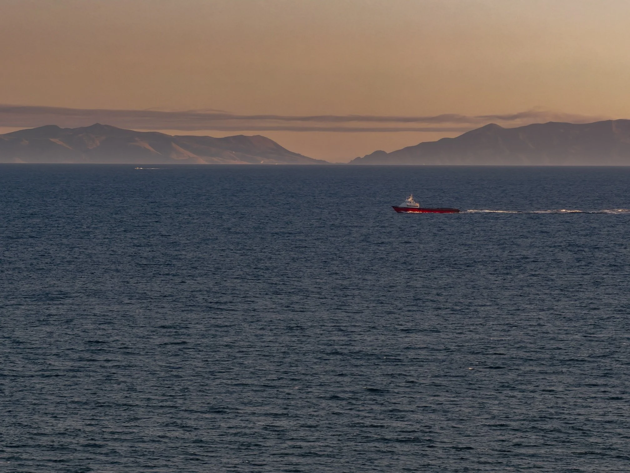 A large ship sailing on the ocean with Two Harbors, Catalina, in the background and a sky with some clouds.