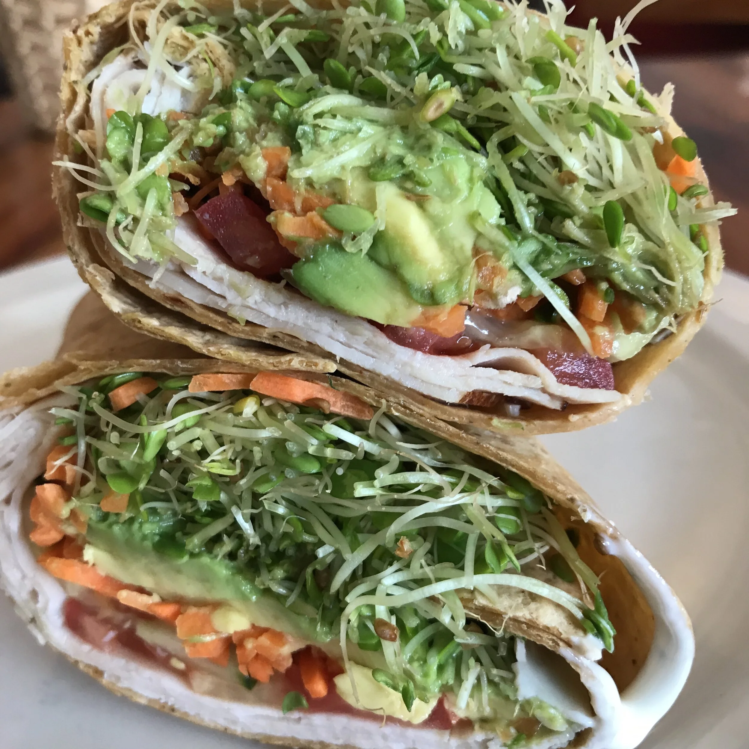 Close-up of a vegetable wrap filled with shredded lettuce, carrots, avocado, sprouts, and other fresh vegetables.