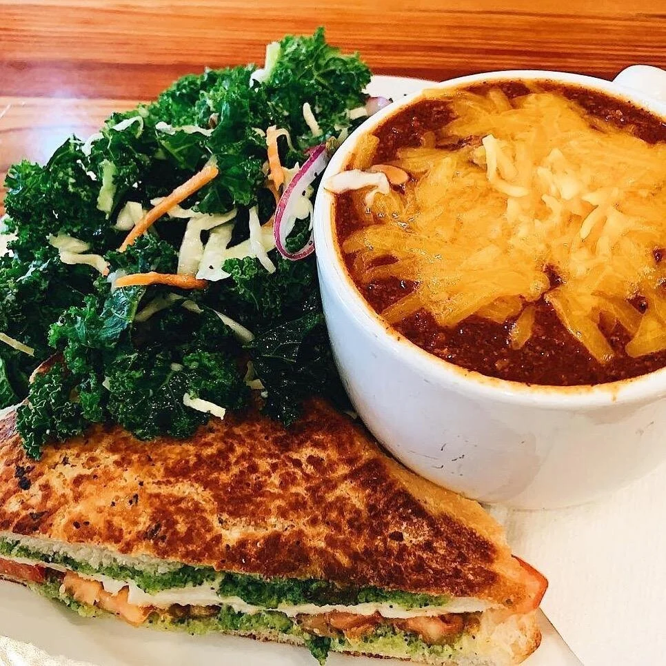 A meal with a grilled sandwich, a side salad, and a cup of baked chili topped with shredded cheese.