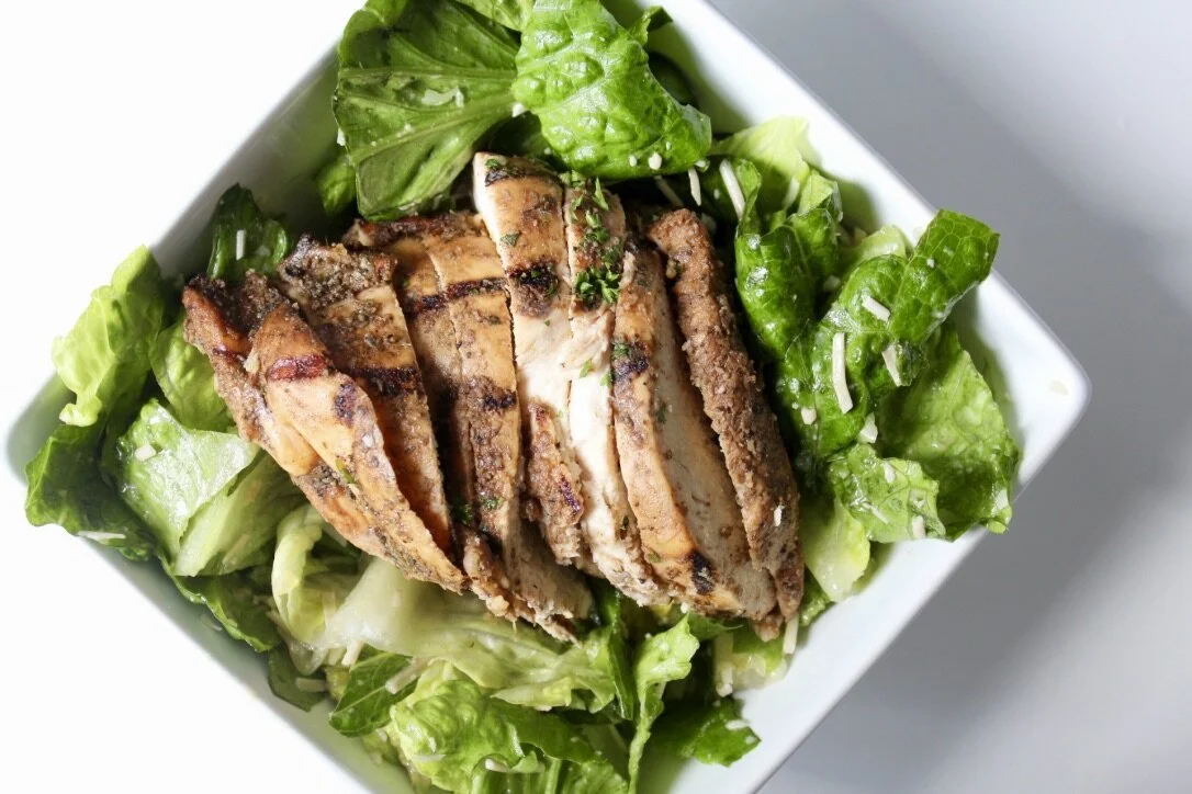 Grilled chicken served on a bed of green lettuce and leafy greens in a white bowl.