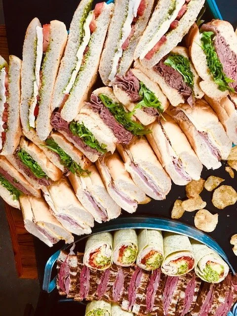 Assorted cut sandwiches and wraps with lettuce, meat, and bread, arranged on a tray with some chips.