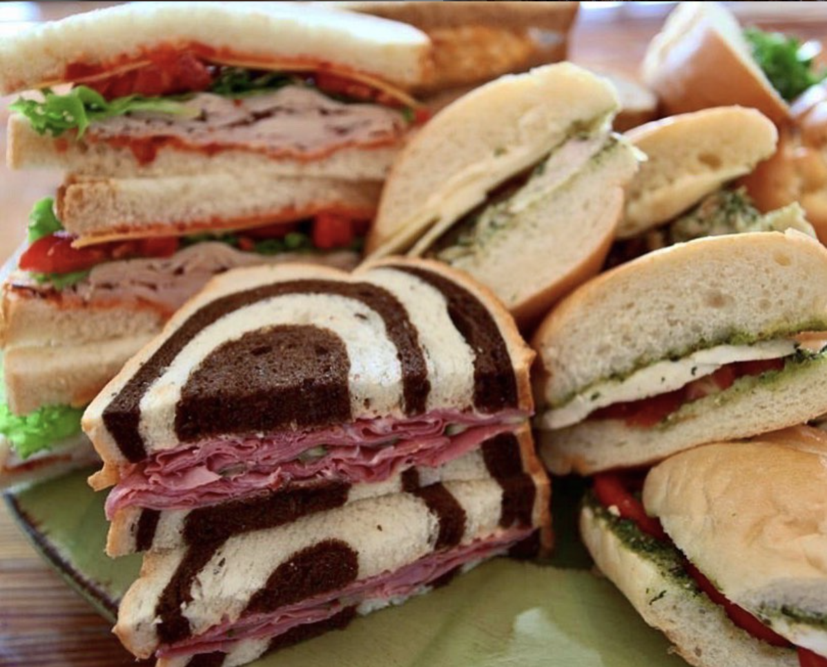 Assorted sandwiches on a plate, including caprese, turkey, ham, and veggie sandwiches, with a zebra cake slice in the foreground.
