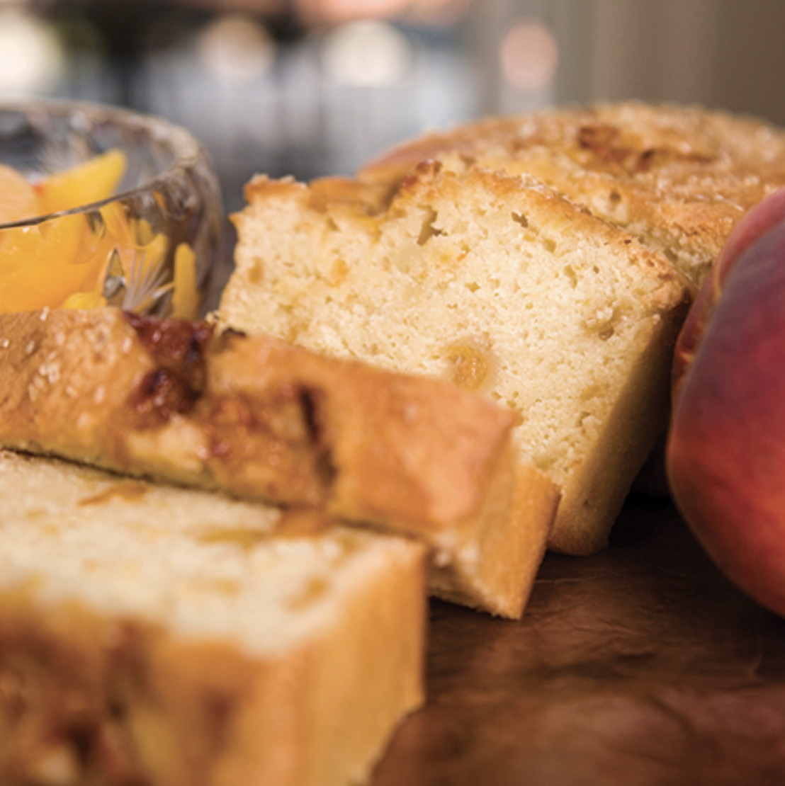 Sliced peach pound cake with a bowl of sliced peaches nearby.