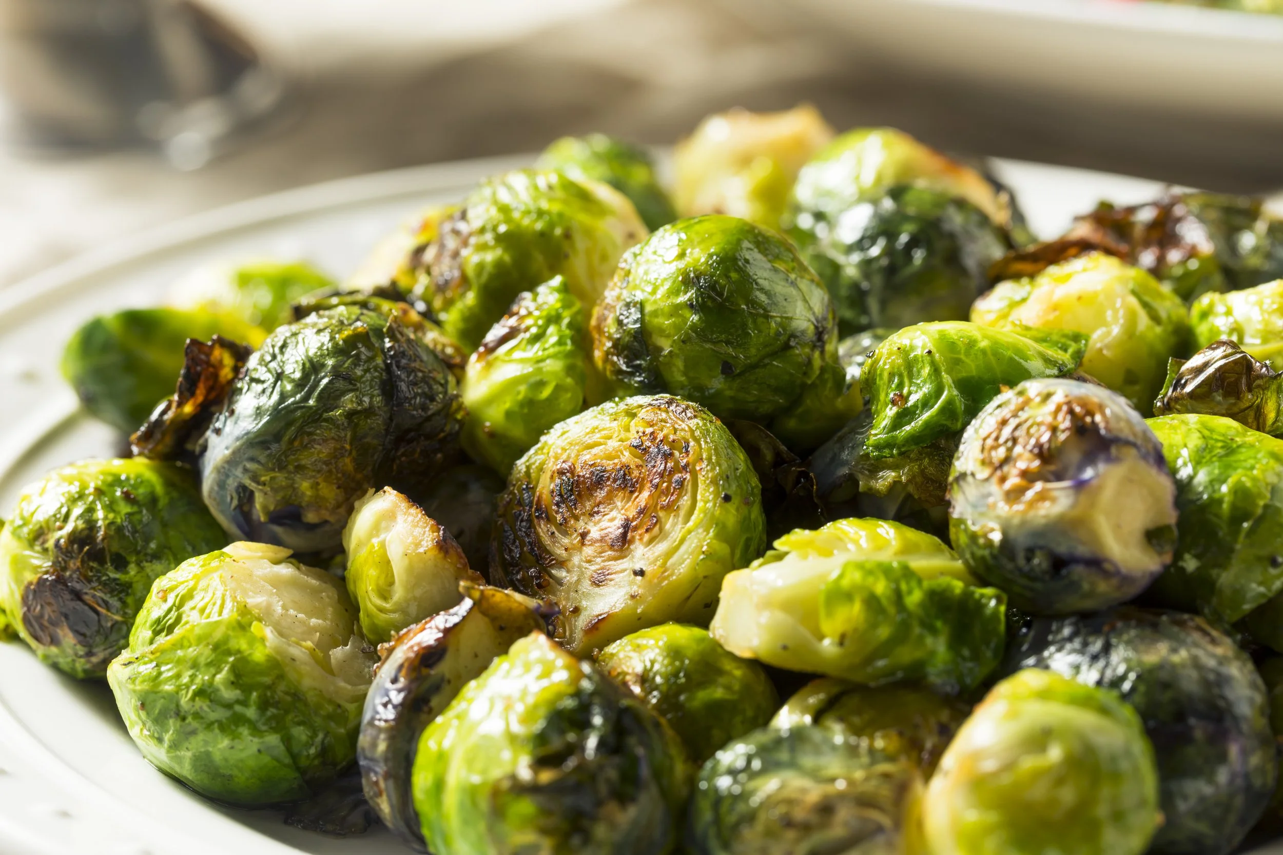 Close-up of roasted Brussels sprouts on a white plate, showing their charred and crispy edges.