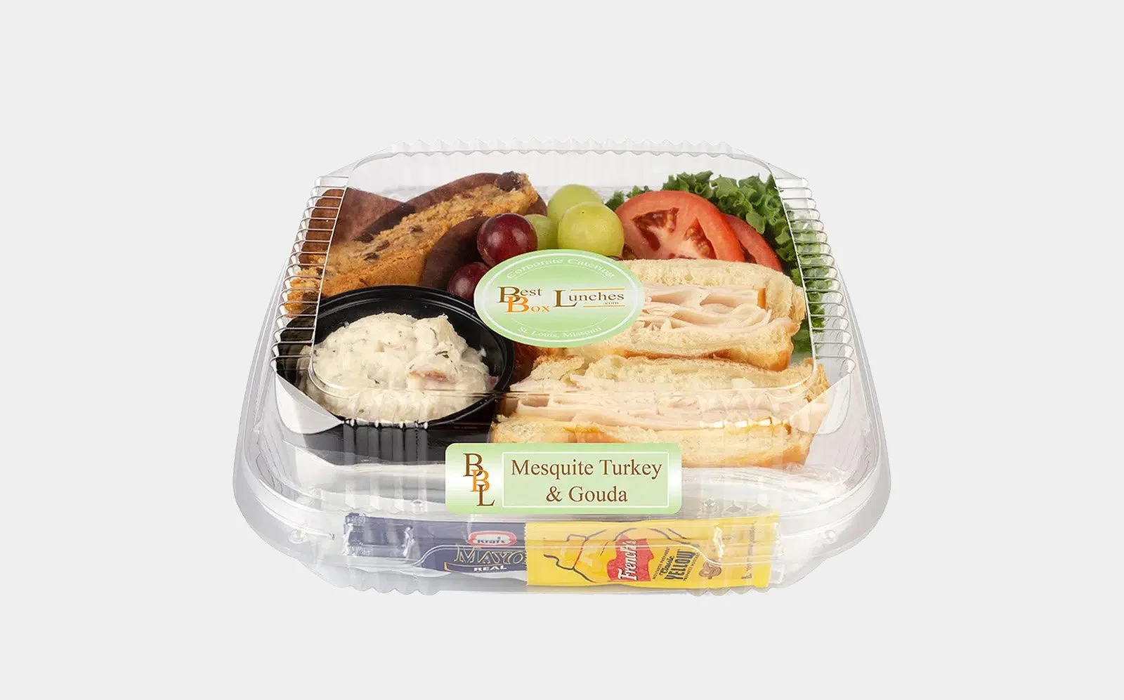 Pre-packaged lunch container with mesquite turkey and gouda sandwiches, grape tomatoes, lettuce, cookies, grape, potato salad, mayonnaise, and a small packet of mustard.
