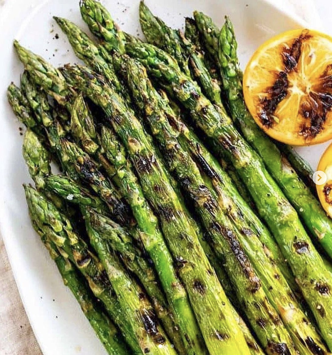 Grilled asparagus spears with char marks, served with lemon halves on a white plate.